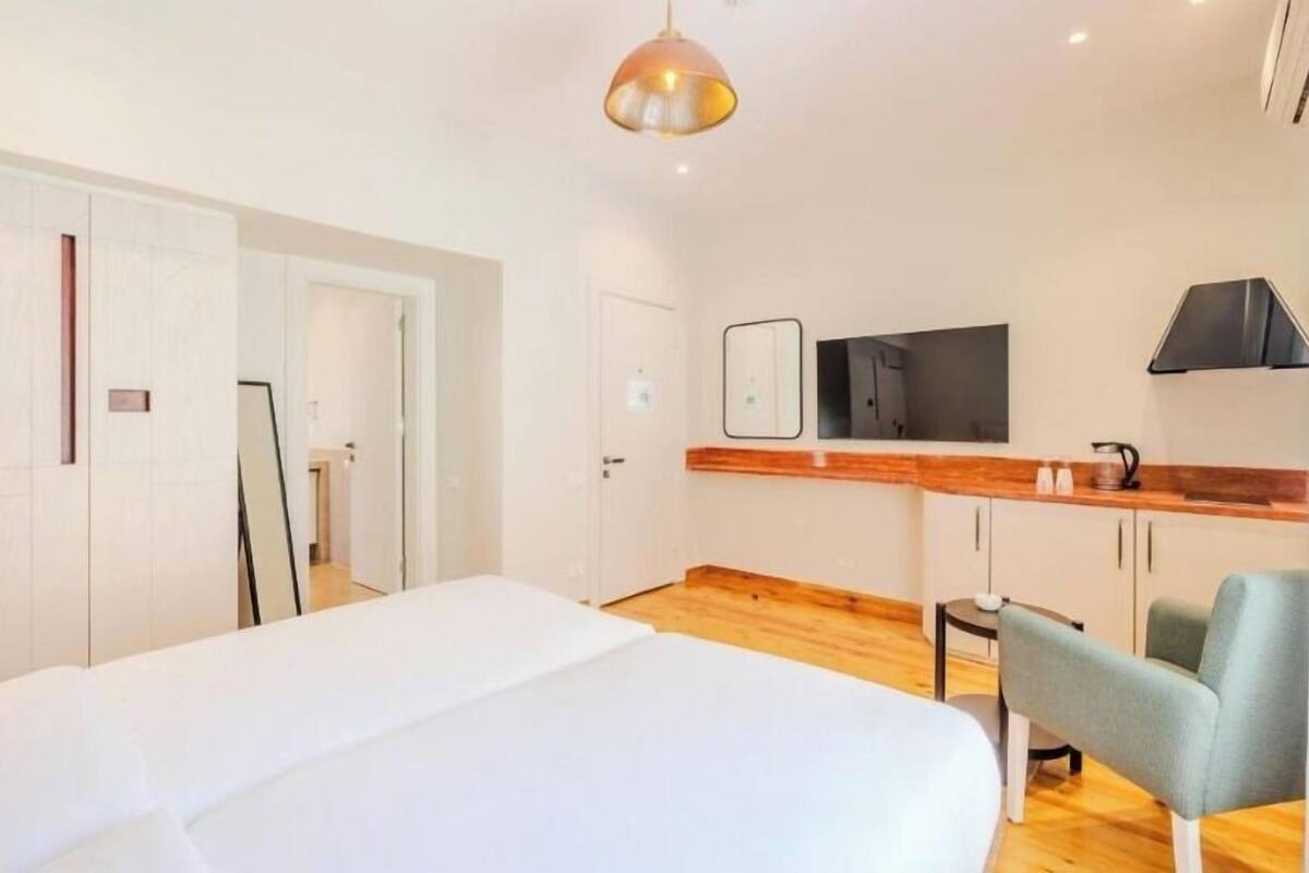 Una habitación de hotel moderna con cama, kitchenette pequeña, televisor y espejo.