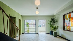 A spacious hallway with a staircase, potted plants, and a large window with a view of buildings. - Longchamps Hotel (Cairo)
