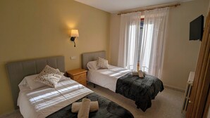 Et hotelværelse med to senge, et natbord, en vægmonteret lampe og et vindue med let gardin.