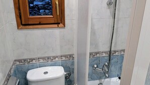 Et badeværelse med toilet, bruser og en dekorativ træpanel over toilettet.