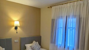 Et hotelværelse med to senge, et natbord, en lampe og et vindue med lette gardiner.