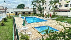 Área de piscina no terraço com duas piscinas, rodeada por espreguiçadeiras e palmeiras.