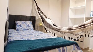 Um quarto com cama, rede, guarda-roupa e mesa de cabeceira.
