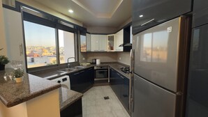 A modern kitchen with granite countertops, stainless steel appliances, and a view of the city through large windows. - Modern fully furnished 4-Room apartment (Amman)