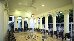 Un vaste espace intérieur avec des rangées de chaises et de tables, des colonnes blanches et un ventilateur de plafond.