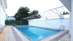 Une piscine intérieure dotée d’un toit en verre, entourée d’un mur blanc et d’une haie verte.