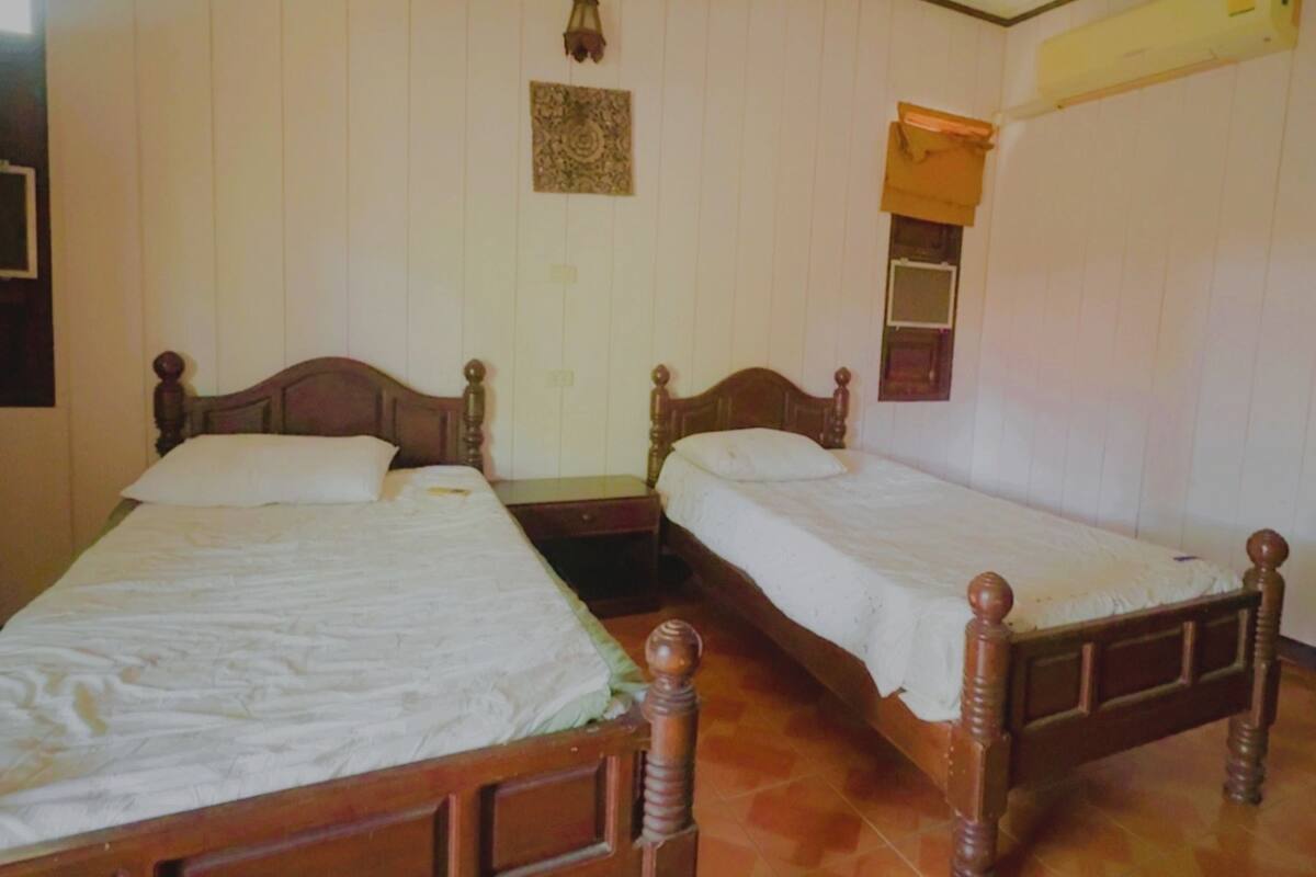 Una habitación con dos camas de madera, cada una con cabecera y piecera de madera, y una mesita de noche pequeña.