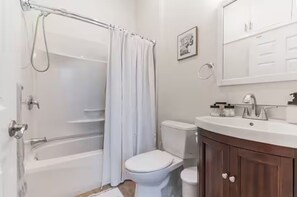 A bathroom with a bathtub, toilet, and vanity with a mirror. - Heart of Downtown OC- Steps to Shopping, Eating, Beach, Boardwalk. On Asbury (Ocean City)