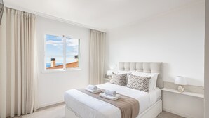 Et pænt indrettet soveværelse med en stor seng, et vindue med gardiner og et natbord med en lampe.