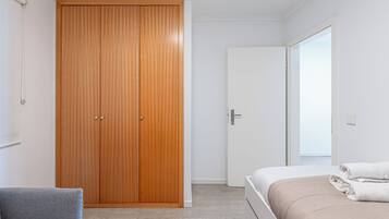 Un dormitorio con un armario de madera, una cama con una manta color beige y un sillón gris.