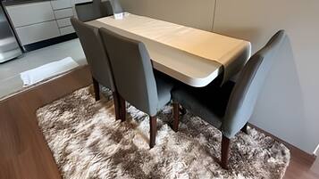A modern dining area with a wooden table and grey chairs, a fluffy rug, and a kitchen in the background.