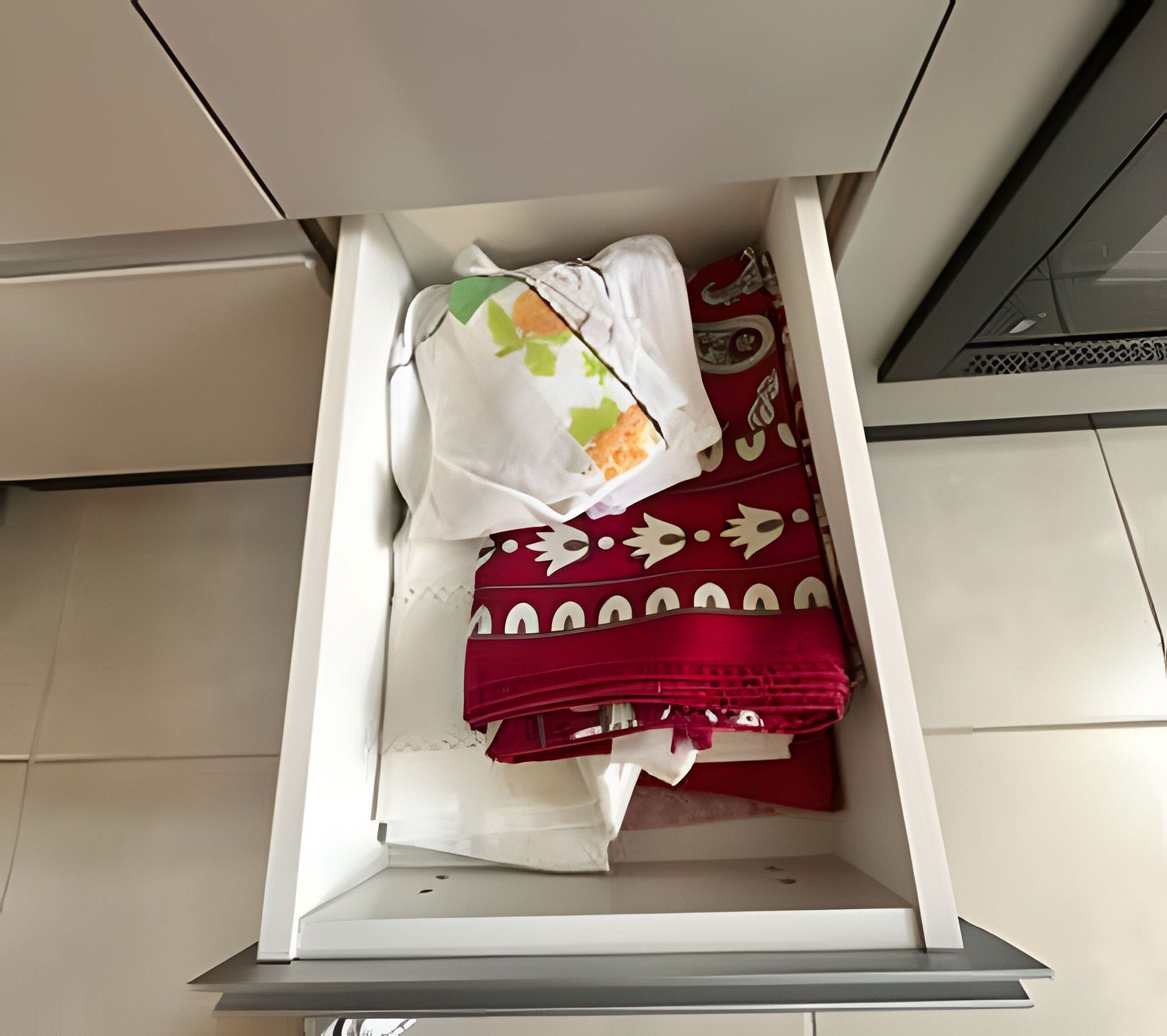 A drawer with neatly folded clothes, including a white garment with a leaf pattern and a red garment with white designs.