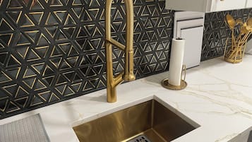 A kitchen with a gold faucet, black geometric backsplash, and a marble countertop.