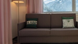 A brown sofa with two decorative pillows, a wooden chair, and a window with a view of snow-capped mountains. - Pitztal Living (Jerzens)