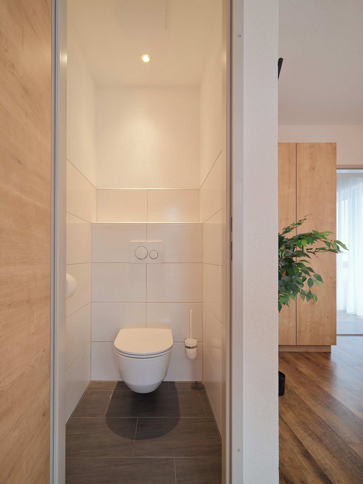 Un baño moderno con inodoro blanco, un espejo pequeño y un dispensador de papel higiénico en la pared.