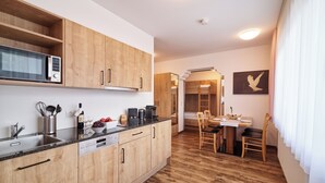 A compact kitchen with wooden cabinets, a microwave, and a dining area with a table and chairs. - Pitztal Living (Jerzens)