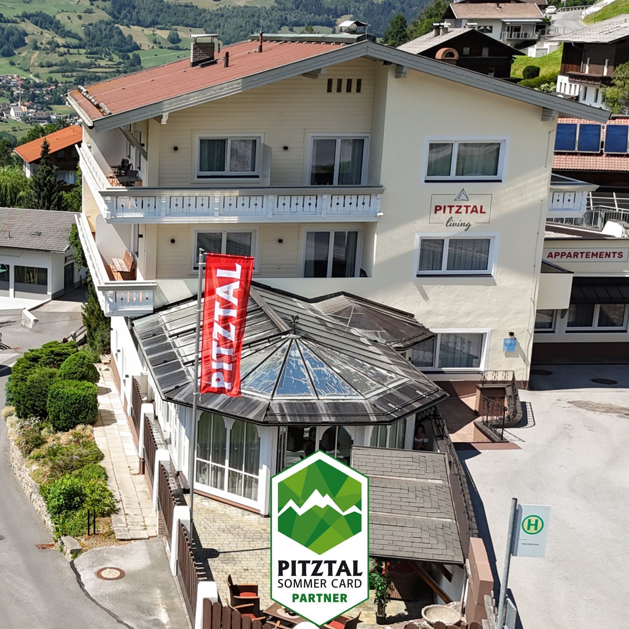 Un edificio de varios pisos con un letrero que dice 'PITZTAAL living' y un logotipo de 'PITZTAAL SOMMER CARD PARTNER'.