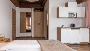 A hotel room with a bed, a wooden ceiling, a kitchenette with a microwave, and a wardrobe. - Pitztal Living (Jerzens)