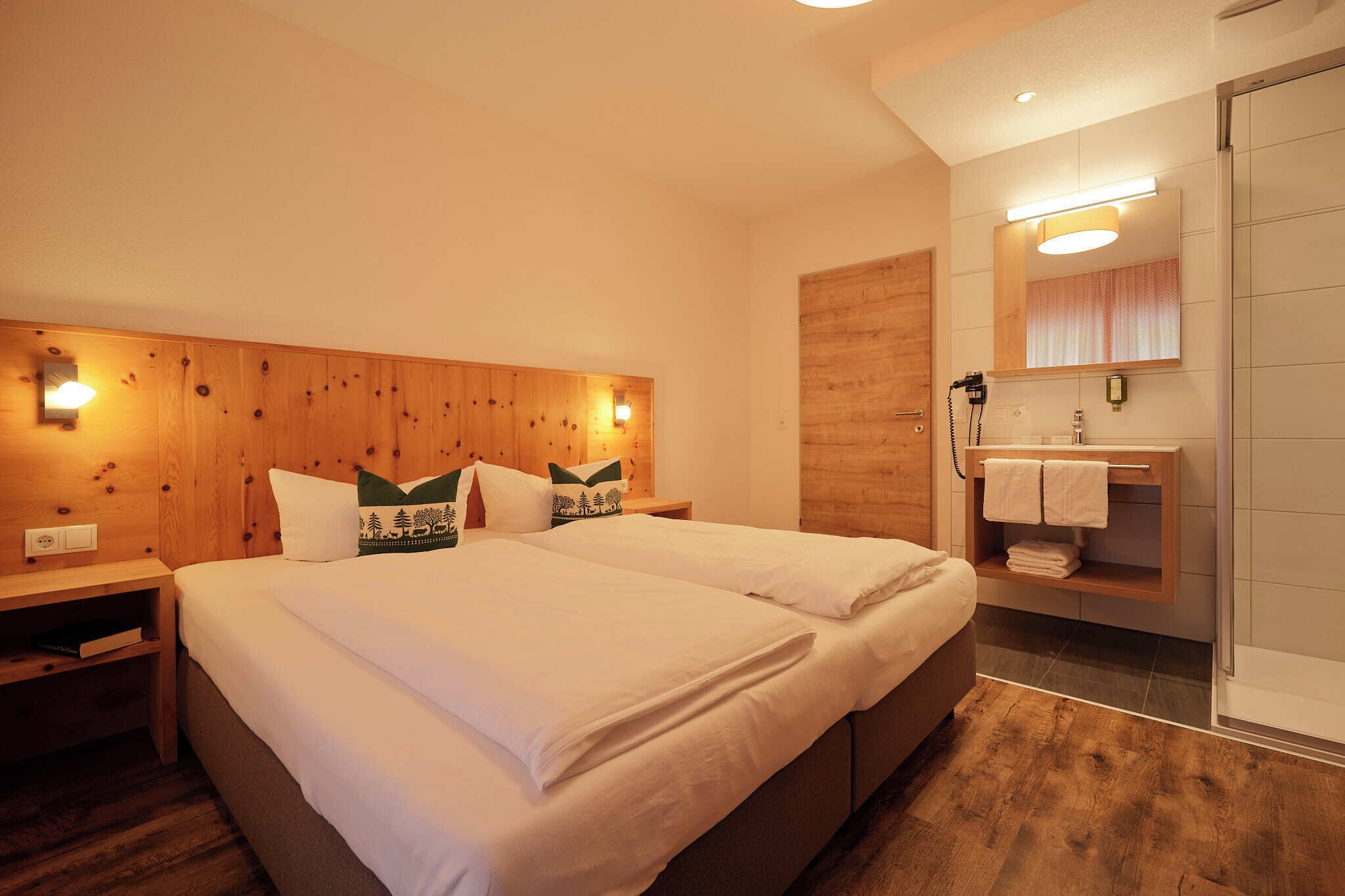 A double bed with white linens, wooden headboard, bedside tables, and a wooden wall panel.
