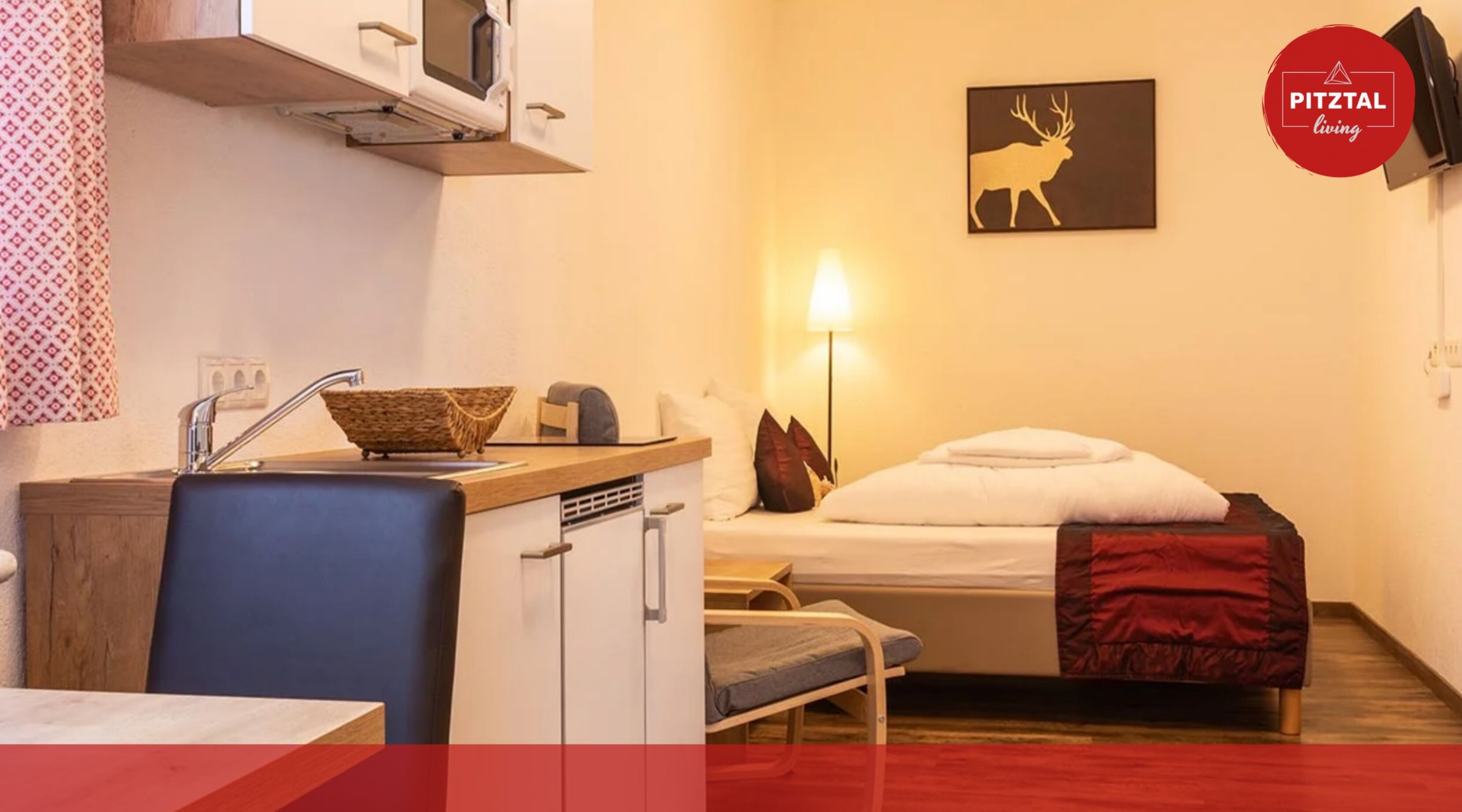 Habitación de hotel compacta con kitchenette, cama individual, lámpara de noche y televisor montado en la pared.
