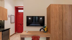 Une pièce de taille modeste, avec un bureau en bois, une chaise rouge, un téléviseur et une porte rouge.