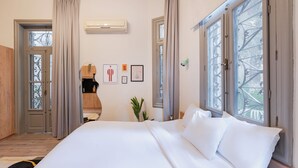 Une chambre d’hôtel avec un grand lit, une armoire en bois, une petite table avec une plante et une fenêtre donnant sur l’extérieur.