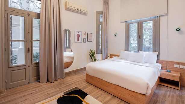 Une chambre à coucher avec un grand lit, un plancher en bois, une fenêtre avec des rideaux et un climatiseur fixé au mur.