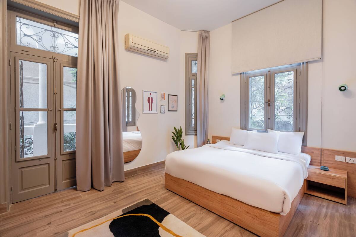 Un dormitorio con una cama grande, suelo de madera, una ventana con cortinas y un aire acondicionado instalado en la pared.