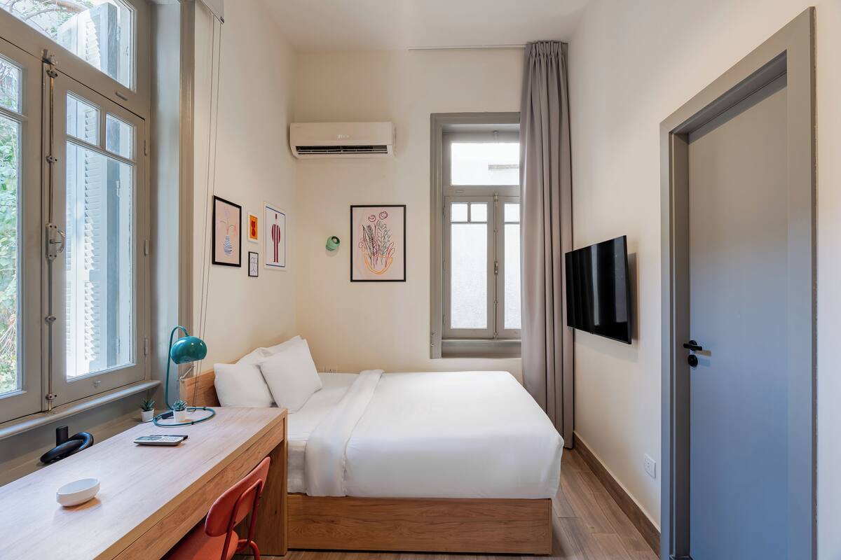 Un dormitorio con cama, escritorio, silla, televisor y ventana.