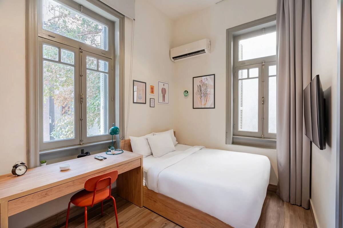 Un dormitorio con cama, escritorio, silla y dos ventanas.