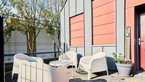A patio with white chairs and a small table, a potted plant, and a building with a red door and large windows. - Paillettes fever, house with karaoke, 3 bedrooms (Croix)