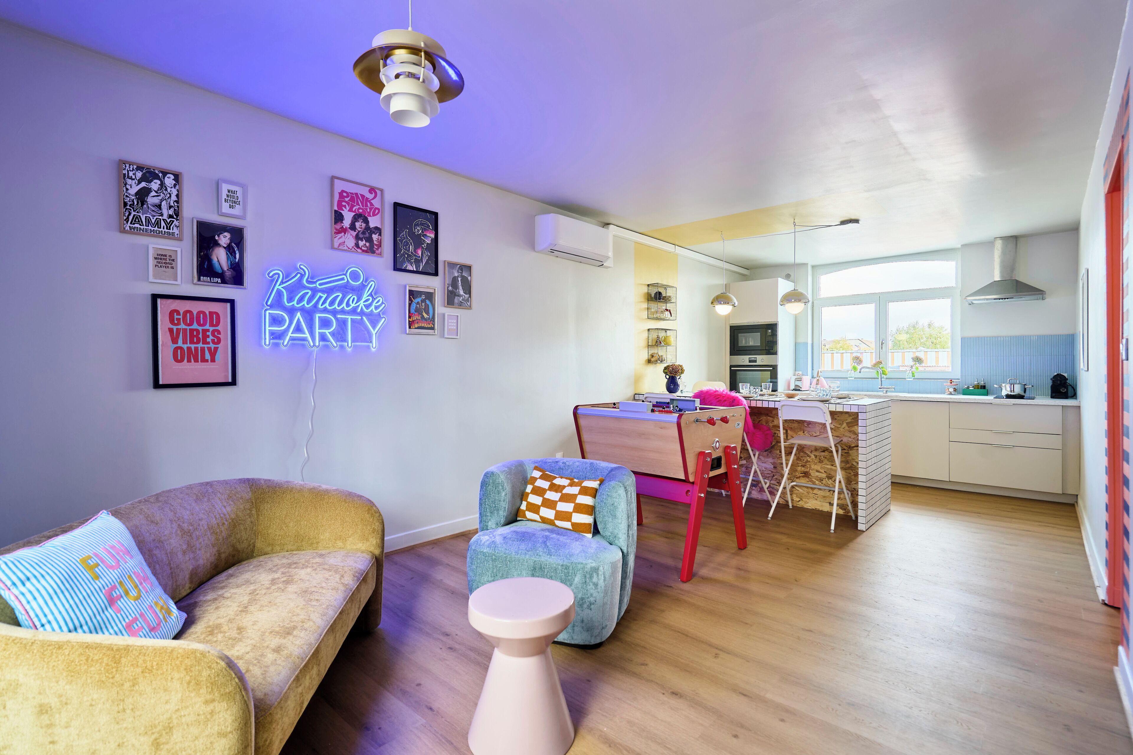 Una sala moderna con sofá, sillón y una mesa redonda, una zona de cocina con mesa de comedor y un letrero de neón en la pared.