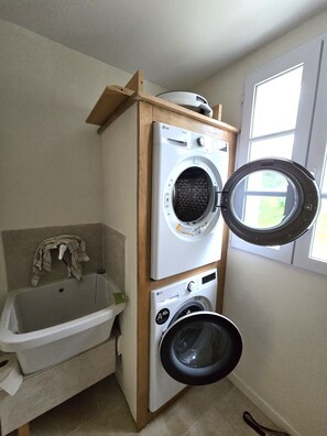 Ein Waschraum mit übereinander gestapelten Waschmaschinen und Trocknern, einer Badewanne und einem Fenster.