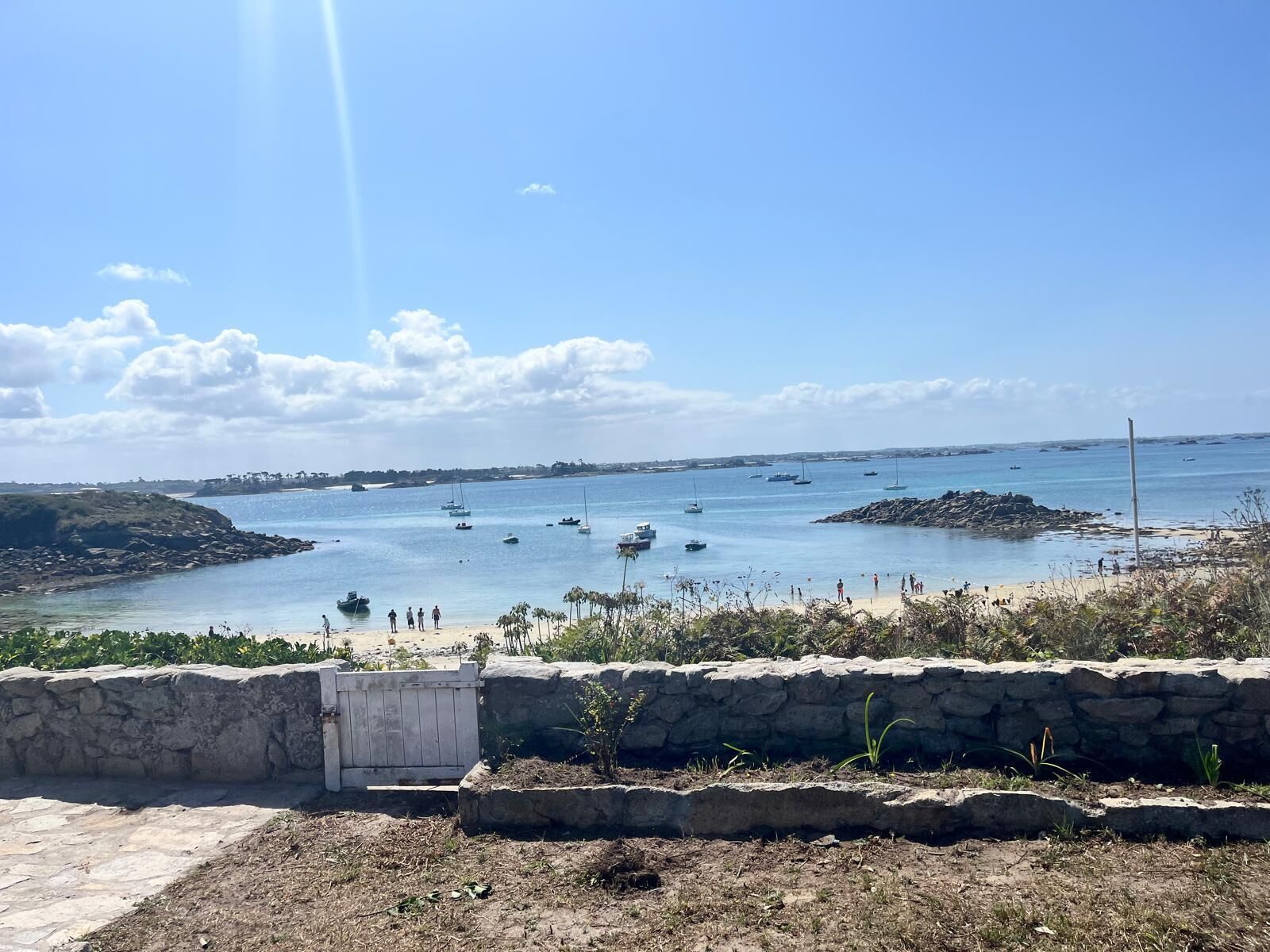A coastal view with boats, a sandy beach, and a stone wall.