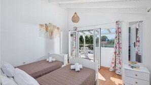 Ein Zimmer mit zwei Betten, einer weißen Kommode, einer Pendelleuchte und einem Balkon mit Blick.