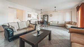 Ein geräumiges Wohnzimmer mit einer Couch, Sesseln, einem Couchtisch und einem Essbereich im Hintergrund.