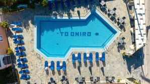 Ein großer Swimmingpool mit dem Namen 'TONIRO', der in die Wasseroberfläche eingearbeitet ist. Um den Pool herum befinden sich mehrere Liegestühle und Tische, die in Reihen angeordnet sind.