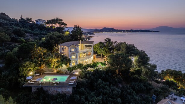 Ein zweigeschossiges Haus mit Swimmingpool, umgeben von Bäumen und mit Blick auf ein Gewässer.
