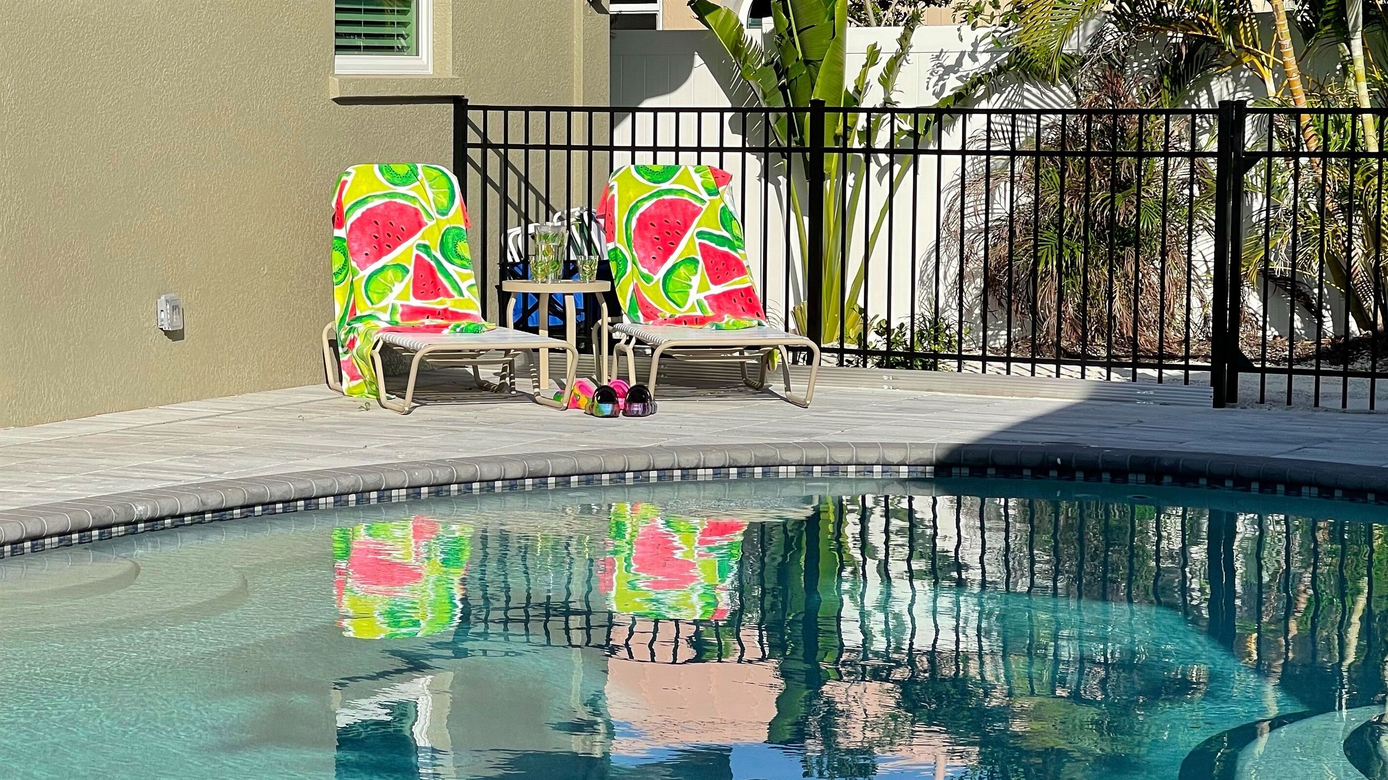 A swimming pool with two lounge chairs and a small table.