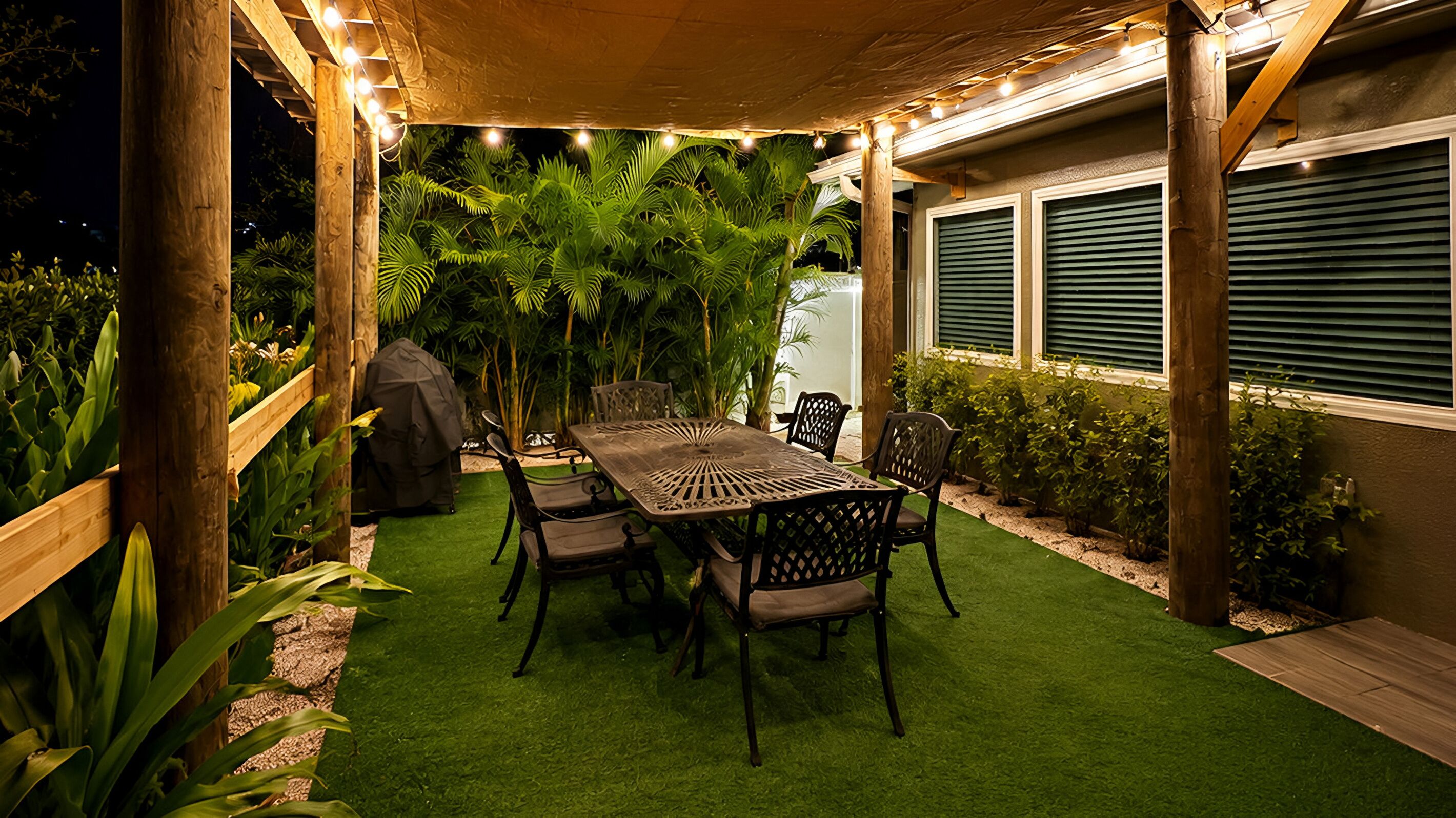 An outdoor patio with a table and chairs, surrounded by greenery and string lights.
