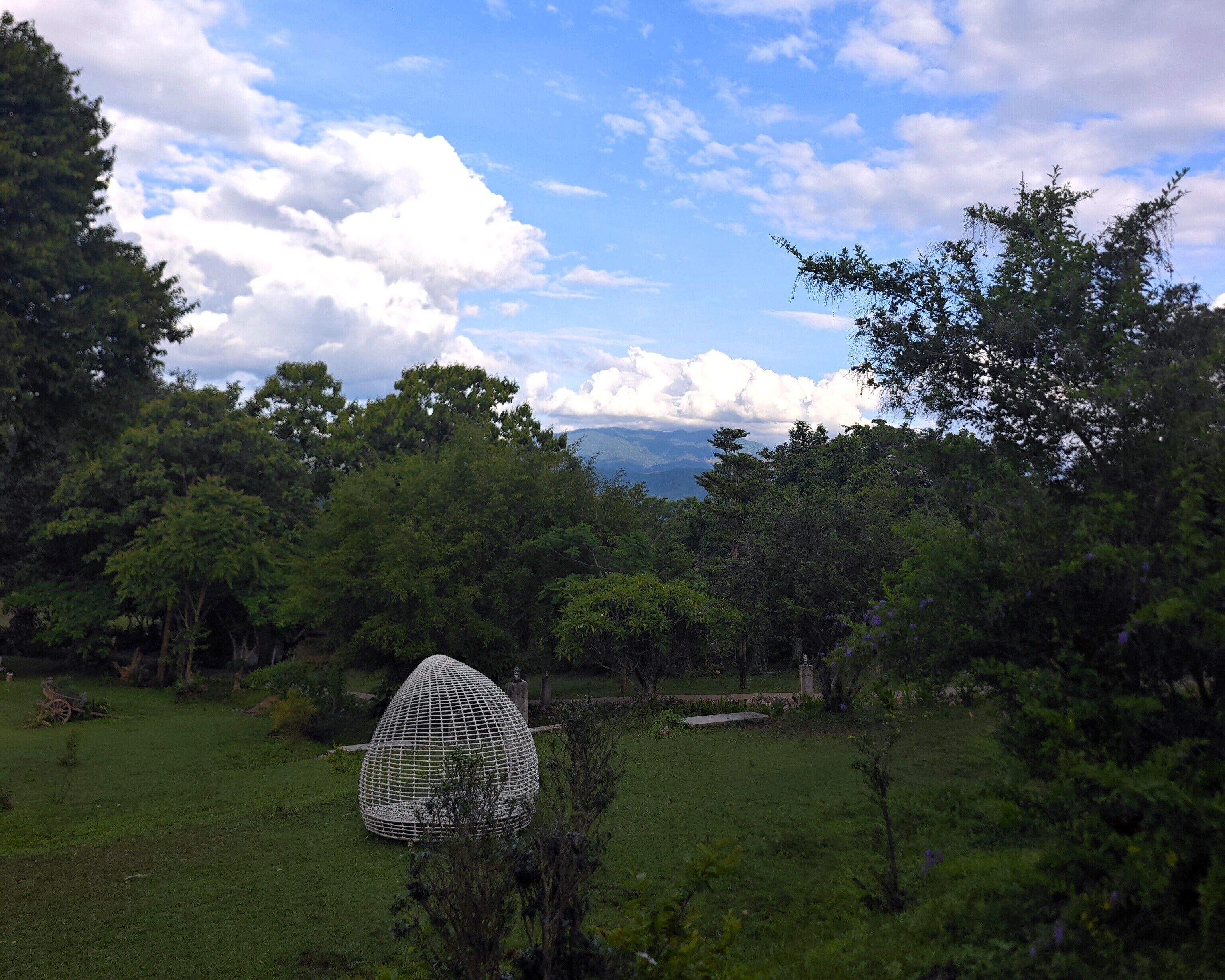 A grassy field with a spherical structure in the foreground and a mountainous landscape in the background.