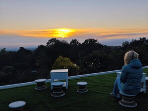 A person sitting on a bench overlooking a sunset with a view of trees and a grassy area. - The Moon Rabbit Resort Pai (Pai)