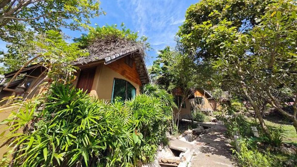 A rustic house with a thatched roof, surrounded by lush greenery and a clear blue sky. - The Moon Rabbit Resort Pai (Pai)
