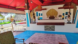A spacious outdoor seating area with a blue carpet, wooden furniture, and a decorative wall with artwork. - The Moon Rabbit Resort Pai (Pai)
