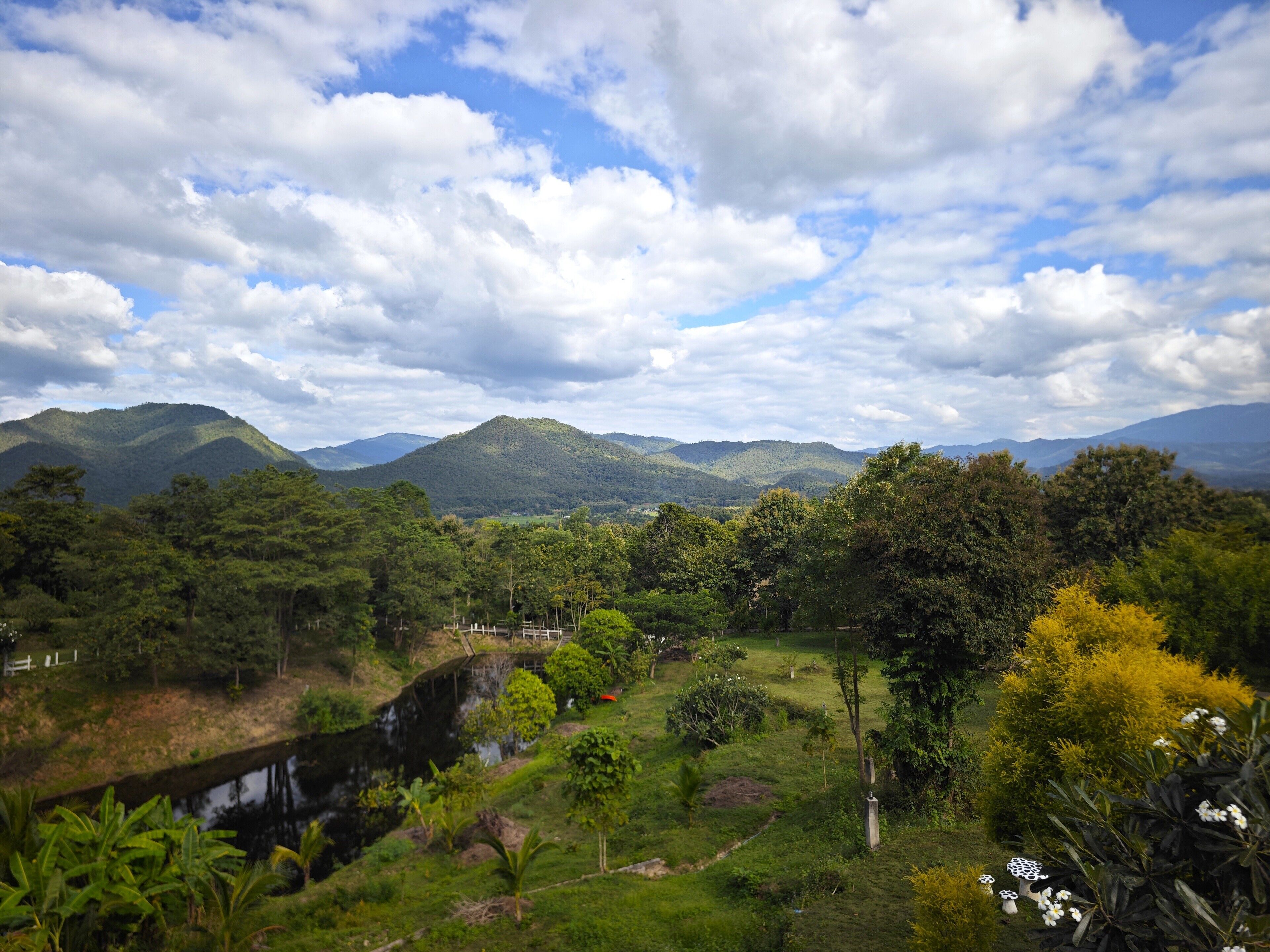 A landscape with a river, greenery, and distant mountains under a partly cloudy sky.