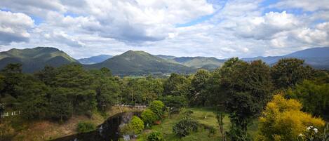Un paisaje con un río, vegetación y montañas distantes bajo un cielo parcialmente nublado.