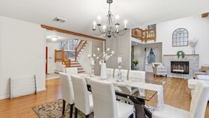 A spacious living room with a dining area, a fireplace, a staircase, and a chandelier.