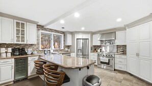 A modern kitchen with white cabinetry, a central island with bar stools, stainless steel appliances, and a stone backsplash.