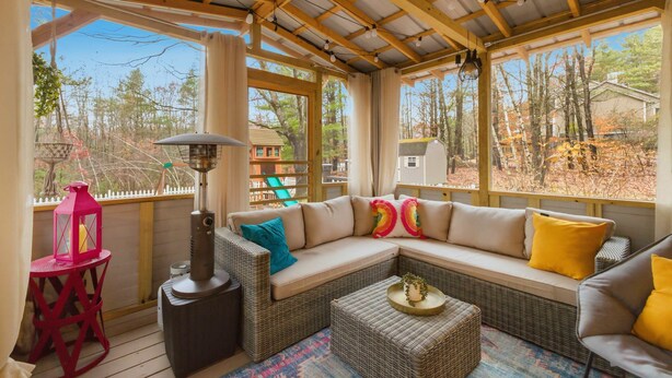 A covered outdoor seating area with a sofa, cushions, a table, and a lantern.