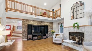 A spacious living room with a fireplace, a large TV, and a balcony.